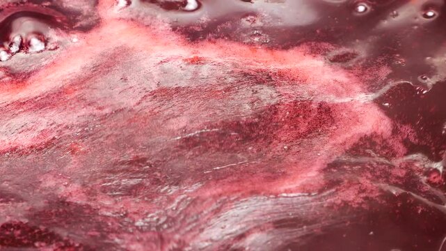 Boiling red currant jam bubbles in a saucepan during the home preparation process. Fresh berry confit cooks on the stove following a traditional recipe. Thick red jelly with small bubbles simmer.