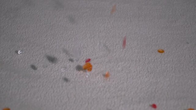 A close-up of small colorful beads falling and scattering against a gray background captured in motion with slow motion effect.