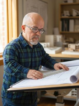 Professional architect with dwarfism working on technical blueprints at drafting desk illustrating urban design planning