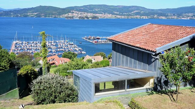 High-angle view of a modern house with zinc metal cladding overlooking the Vigo estuary marina in Galicia, Spain. Captures contemporary architecture, coastal properties, and luxury harbor assets.