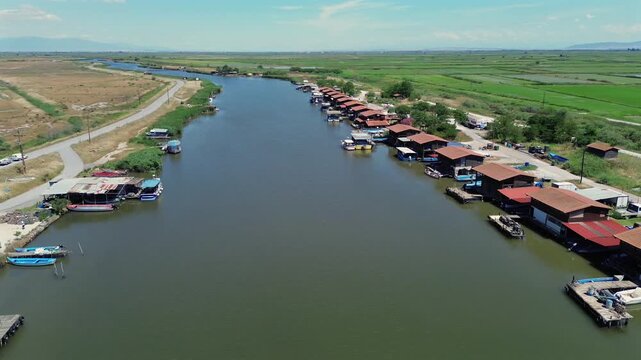 Cinematic drone view flying over a winding river revealing a long row of traditional stilt fishing huts and small boats docked by the waterfront.