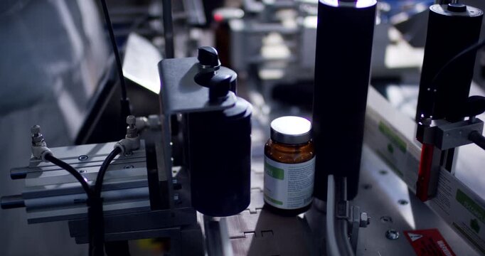 Automated packaging machine labeling a brown glass medicine bottle on a conveyor belt in a factory