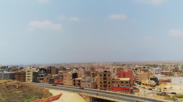 Camera pans across Dakar urban skyline above elevated highway in dusty haze