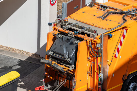 Rear loader garbage truck empties waste containers during municipal collection route urban area. Modern sanitation equipment support recycling, waste management public hygiene essential city services