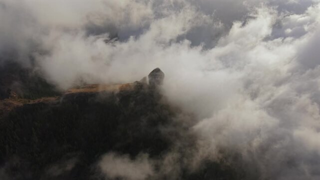 Dramatic aerial view of Roque Nublo, a volcanic rock formation, emerging through cinematic clouds on the island of Gran Canaria, Spain