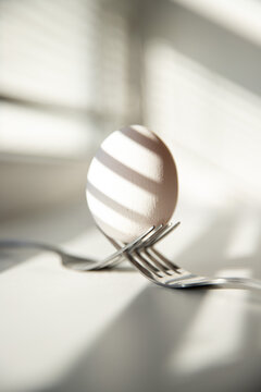 Single white egg balancing on fork near window.