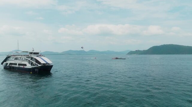Drone skims the water past a ferry to reveal parasailing activity in Thailand.