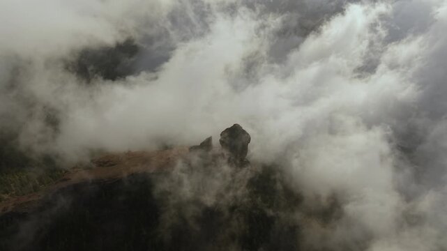 Breathtaking aerial footage capturing the majestic Roque Nublo, a volcanic rock on Gran Canaria, piercing through a sea of moving clouds