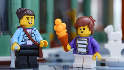 Obraz premium Tambov, Russian Federation - June 24, 2026 Two Lego minifigures standing on a city street, with one holding a large ice cream cone near another figure holding a crutch.