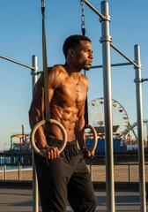 Fototapeta premium Muscular Black Man Training with Gymnastic Rings at Outdoor Beach Gym During Golden Hour Sunset