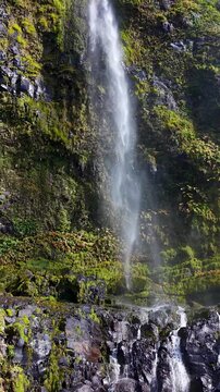 Detailed close up footage of Poco do Bacalhau waterfall flowing over moss covered volcanic rocks with sparkling water and lush vegetation on Flores Island Azores Portugal