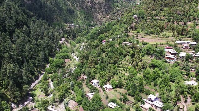 Mountain village spreads across green hillsides beside dense forest in Katha Piran, Kashmir, Pakistan