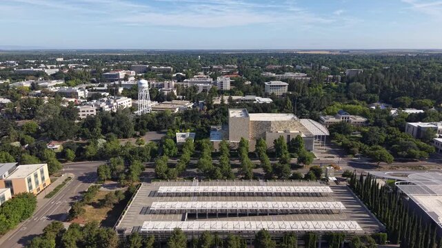 Ascending drone shot of the University of California, Davis campus, showing the Robert and Margrit Mondavi Center for the Performing Arts and the surrounding cityscape on a sunny day