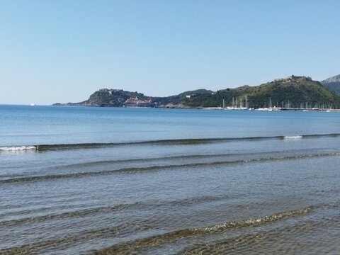 Vista panor&aacute;mica de la costa y el puerto de Porto Ercole desde una playa de aguas tranquilas, Toscana, Italia.
