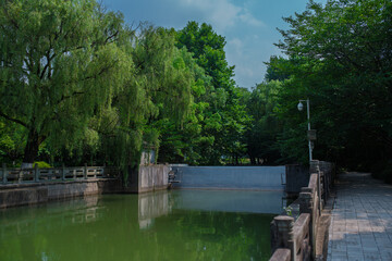 Fototapeta premium Ship lock and stone paved walkway surrounded by lush green weeping willows in Baita Park in Hangzhou
