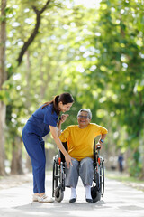 Obraz premium Caregiver assisting senior woman in wheelchair outdoors, providing empathetic support and companionship during a relaxing walk in a green park environment