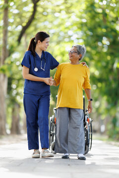 Medical professional assisting a senior asian woman walking outdoors in a park, providing care and support for rehabilitation and independent living