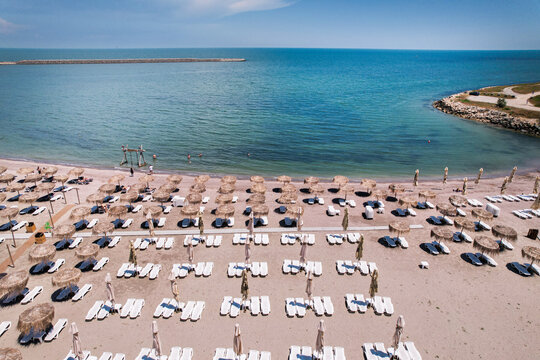 Aerial top down view of an organized sandy beach resort with rows of straw umbrellas and white sun loungers near the sea. Aerial top down view of rows of straw umbrellas and sun loungers on a sandy be