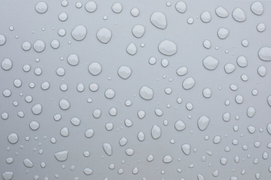 Gouttes d'eaude pluie perlant sur une surface m&eacute;tallique grise, un capot de voiture, une planche de bois contre-plaqu&eacute;e.