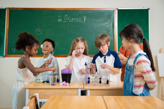 Diverse elementary school children using droppers and test tubes during a chemistry science experiment in classroom. Students collaborating on scientific laboratory project with colorful liquids.