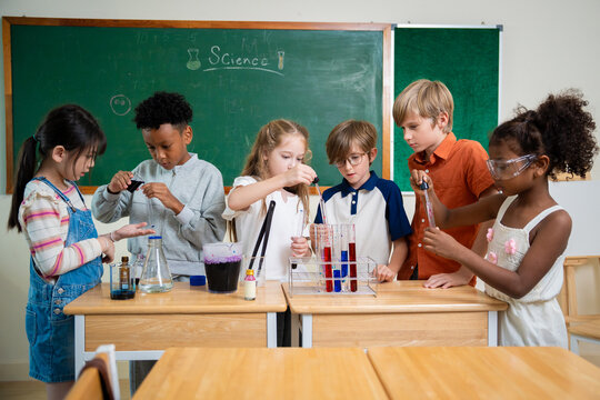 Diverse elementary school children using droppers and test tubes during a chemistry science experiment in classroom. Students collaborating on scientific laboratory project with colorful liquids.
