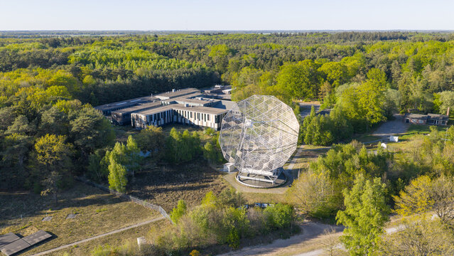 Aerial view of the Westerbork Synthesis Radio Telescope featuring its large parabolic dish antenna surrounded by dense forest and research buildings in Zwiggelte, Drenthe, Netherlands.