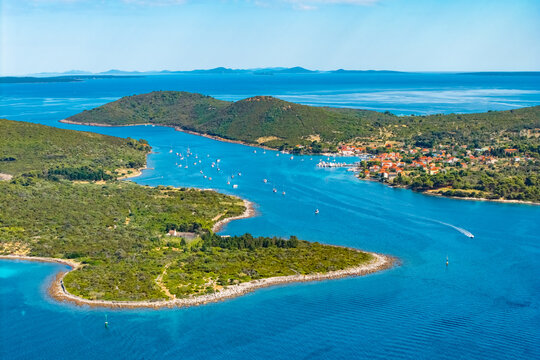 village of Ilovik, Croatia, with traditional red-roof houses surrounded by olive groves and dry stone walls. The narrow channel is filled with white sailboats