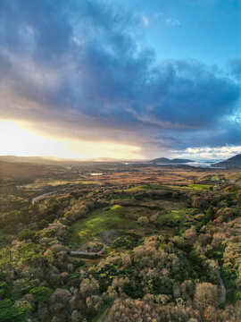Aerial view of the Howth peninsula landscape with rolling green hills, dense woodland, and coastal vistas under a dramatic sunset sky in Dublin, County Dublin, Ireland.