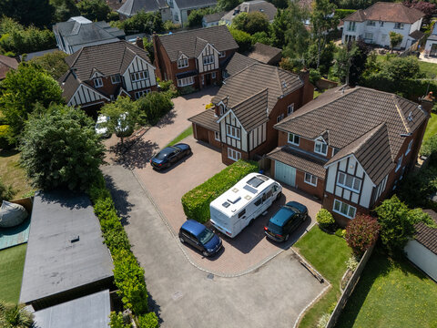 Aerial view of a luxury campervan parked in a residential cul-de-sac surrounded by detached houses, manicured lawns, and parked cars in London, England, United Kingdom.