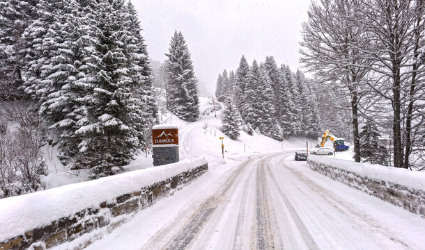 Verschneite Passstra&szlig;e am Ortsausgang von Dam&uuml;ls in Richtung Au mit Steins&auml;ule und gemauerter Br&uuml;cke bei Schneefall, Vorarlberg, &Ouml;sterreich