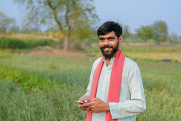 Fototapeta premium young indian farmer using smartphone standing at green agricultural field