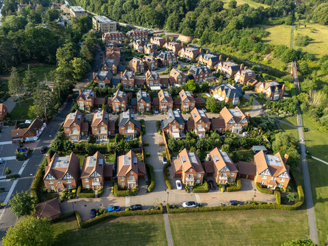 Aerial view of luxury new build homes with red brick facades, dark tiled roofs, and manicured gardens in a quiet residential neighborhood in Maidenhead, England, United Kingdom.