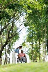Fototapeta premium Caregiver supporting senior woman on wheelchair during an outdoor park walk, providing assistance and companionship, promoting health, mobility, and an active lifestyle