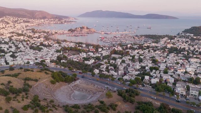 Cinematic aerial drone reveal over historic Bodrum showing ancient Halikarnassos amphitheater medieval Castle of Saint Peter marina with Turkish gulets and Aegean Sea at golden hour Mugla Turkey