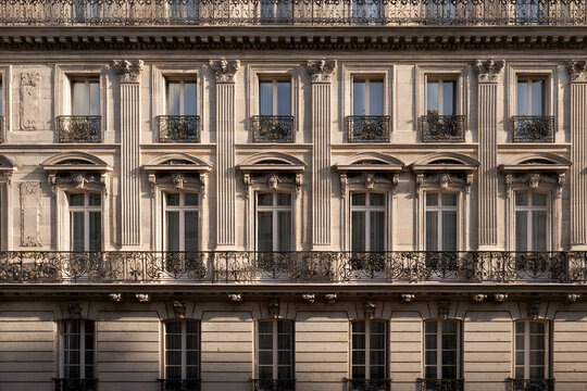Ornate Parisian building facade with wrought iron balconies and dormer windows, bathed in golden hour sunlight, showcasing classic Haussmann architecture.