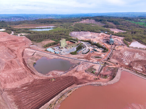 Aerial view of a large industrial quarry site featuring deep red earth, sediment ponds, processing facilities, and heavy machinery in Checkley, England, United Kingdom.