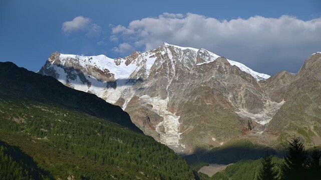 Monte Rosa glacier and east face above Macugnaga in the Italian Alps, summer mountain landscape with blue sky and clouds approaching the peak