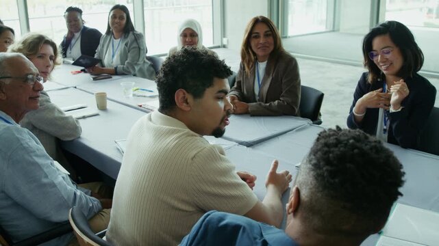 Professionals actively participate in a conference meeting, exchanging ideas and discussing topics around a table. They are engaged in thoughtful conversation, listening to each other's perspectives.