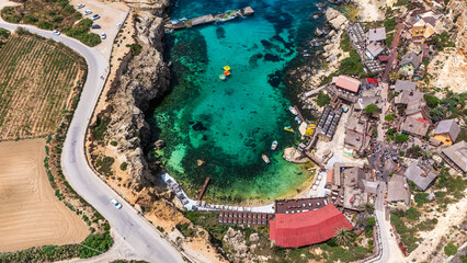 aerial drone view of anchor bay on south malta coast with crystal clear Mediterranean Sea water and boats with cliffs surrounding in summer © STJMEDIA