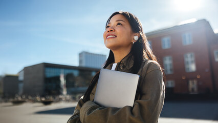 Fototapeta na wymiar Young female student commuting to university smiles while holding laptop