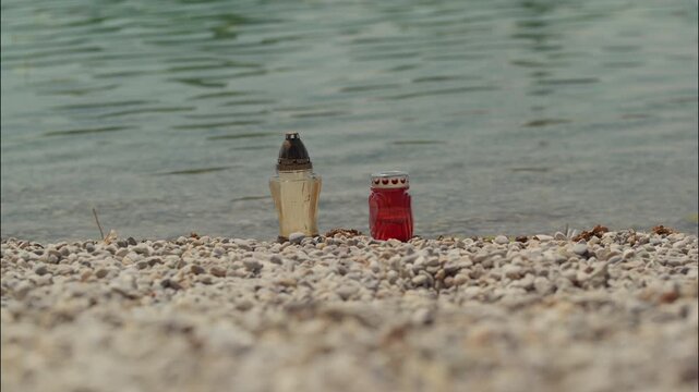 Two memorial candles placed on the pebbled shore of Jarun Lake beside the water in Zagreb Croatia.