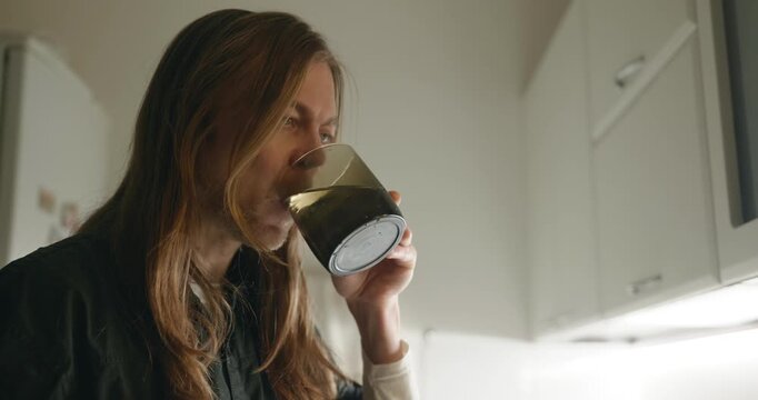Caucasian man drink hot water in evening. Single male is drinking tea at kitchen at home. 4K 10-bit