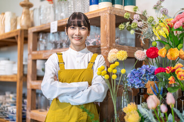 Obraz premium Smiling female florist standing with crossed arms at camera arranging beautiful colorful artificial flowers in retail boutique, Small business SME owner, home decor shop management, creative concept