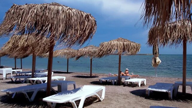 Tropical beach resort scene with thatched straw umbrellas, white sun loungers, and two girlsrelaxing on the sandy shore near the sea. 