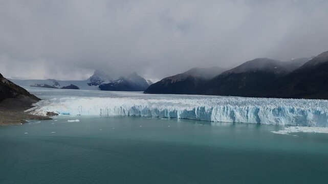 Perito Moreno Glacier spans Argentino Lake in Los Glaciares National Park near El Calafate, Patagonia, Argentina, revealing a vast terminus beneath cloud covered Andean peaks, oblique forward drone