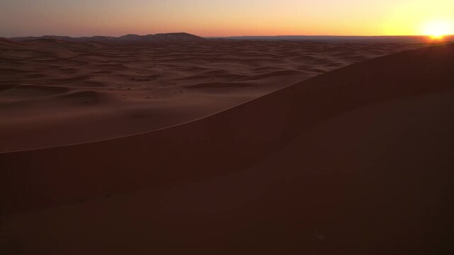 Sunrise illuminates the Erg Chebbi dune sea near Merzouga, Morocco, revealing endless wind sculpted formations and flowing sandy textures across the Sahara, slow drone forward flight shot.