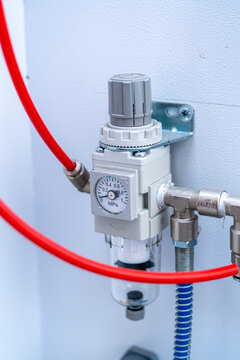 Close-up of pneumatic pressure regulator with gauge and red air tubes mounted on wall
