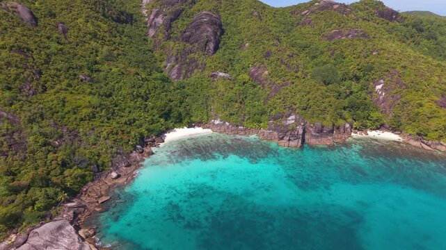 Drone reveal of the isolated Anse Du Riz beach in Seychelles, showing turquoise marine park waters, dramatic granite cliffs, and dense tropical jungle
