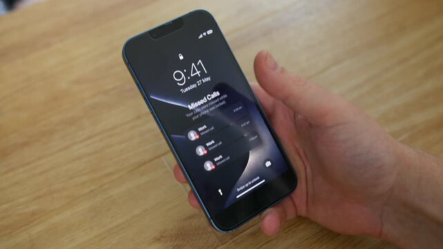 Missed calls from Work appear on a smartphone lock screen while a person holds the device above a wooden table in a close-up shot. Business communication, work life balance, mobile notifications, and