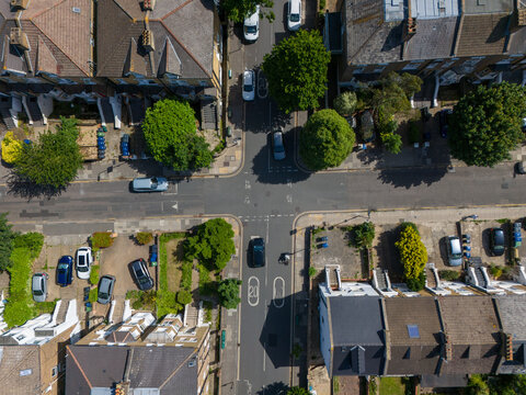 Aerial view of Ealing residential streets with a quiet intersection, parked cars, lush green trees, and classic terraced houses in London Borough of Ealing, England, United Kingdom.